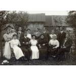 A photo of eight people standing and six people sitting in chairs in front of a building and trees. 