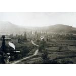 A group of oil derricks. There is a road and fields in front of them and hills in the background.