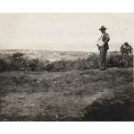 Humphrey Tracy standing on a hill looking at Port of Spain. He is wearing a suit and hat. There are trees and water in the background.