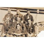 Seven men wearing ties and dark suits sitting in three rows (three, three, and one at the bottom). 