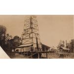 A photo of a covered oil rig set on stilts. There are trees in the background. 