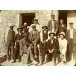 A photo of a group of International Drillers standing and sitting in front of a light stone building with an open doorway. They are wearing suits and vests.