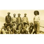 A photo of an International Driller wearing a white shirt, standing next to ten local workers wearing hats.