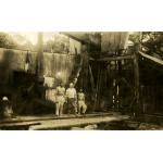 Three men standing in front of an oil rig covered with metal siding. They are standing on a pile of casing.