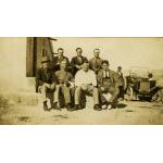 Seven International Drillers sitting on a stone ledge. There are two people in the background with a car.