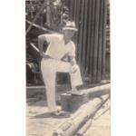 Harry Smith dressed in a white suit and panama hat, with one leg up on a bench.