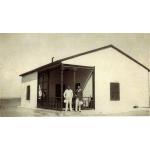 Ross Dyke et un autre foreur debout devant une maison blanche avec une rampe foncée autour du porche, tenant des casques coloniaux blancs.