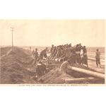 Black and white image of approximately 20 men using large wrenches as levers to connect two large pipeline pieces together in a desert. 