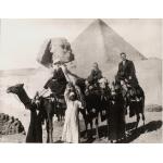 Une photo de M. et Mme Saunders et de leur fils à dos de chameaux. Trois habitants de la région se tiennent debout sur le sol et portent des bouteilles sur leur tête. On aperçoit le Sphinx et une pyramide à l'arrière-plan.