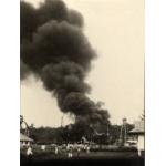 A photo of a group of people watching a cloud of black smoke near a group of oil derricks.