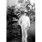 Henry Gregory standing in front of a trees. He is wearing a white suit and pith helmet.