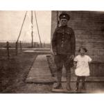 Arthur Brown standing next to Dorothy. He is wearing a military uniform and she is in a white dress. They are standing in front of a wooden building with wooden planks around it. There are derricks in the background.