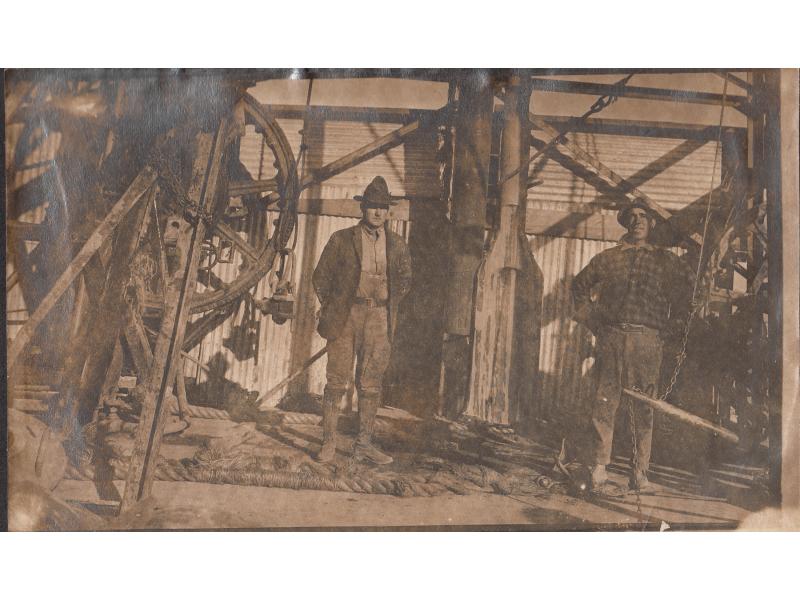 Harry Smith and an unknown man standing in a derrick, next to the drilling bit.