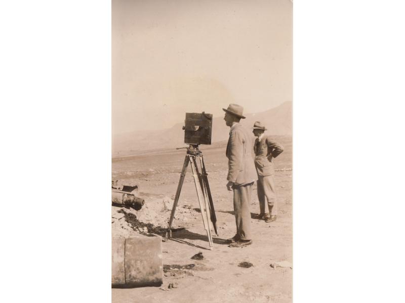 Two men standing in the desert. One is looking at a device, possibly a total station.