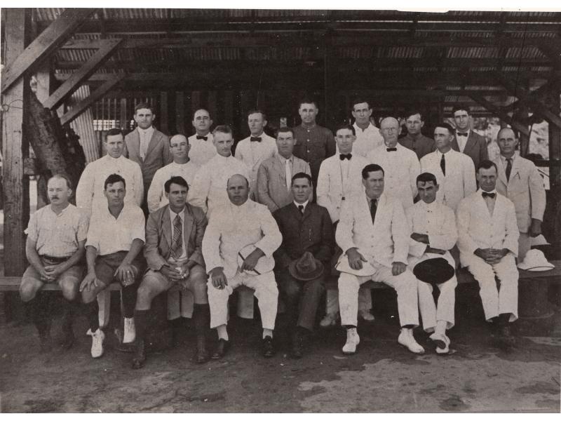 A photograph of a group of International Drillers. They are arranged in three rows, on a platform elevated off of the ground. They are under a roof with wooden supports and metal sheeting.