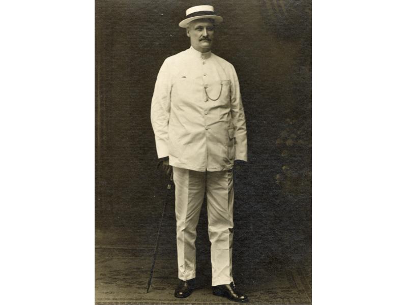 William McRae debout vêtu d’un costume blanc et d’un chapeau de plaisancier. 