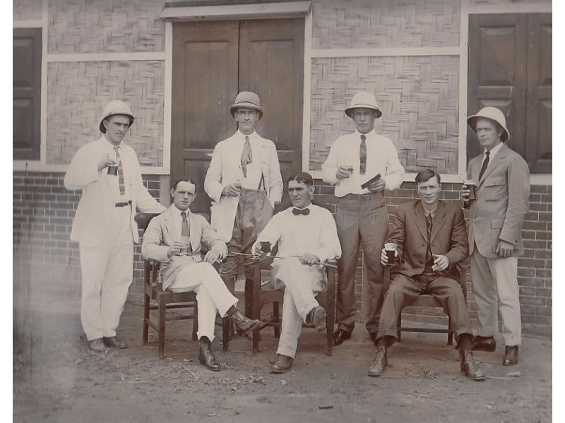 Group of oil drillers in Burma, outside their quarters. They are wearing suits or dress shirts and ties. They all have drinks in their hands.