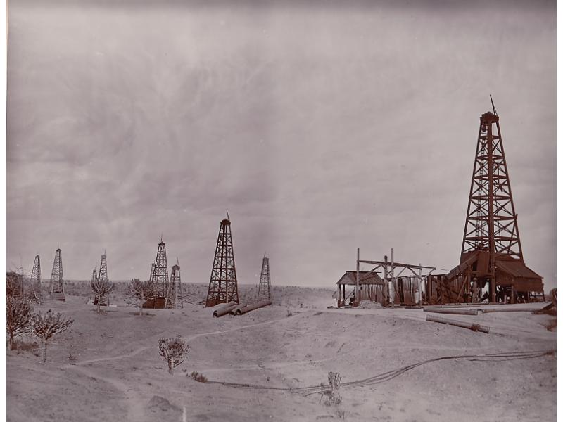 Ten oil rigs in a dirt field. There is casing in front of the rigs and the bottoms are covered.