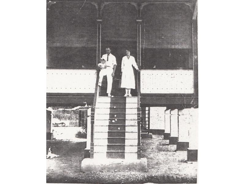 James Brown Sr., holding a small child, standing next to his wife on the steps of their home which is raised off the ground on pillars. 
