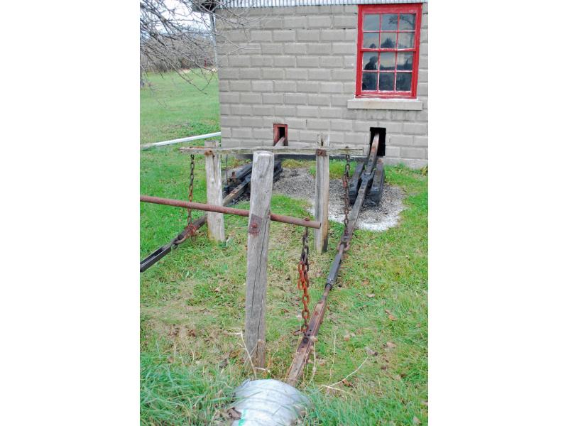 Two wooden slide blocks emerging from holes in a grey, cement-block wall and running into culverts. The chains supporting the lines are rusted.