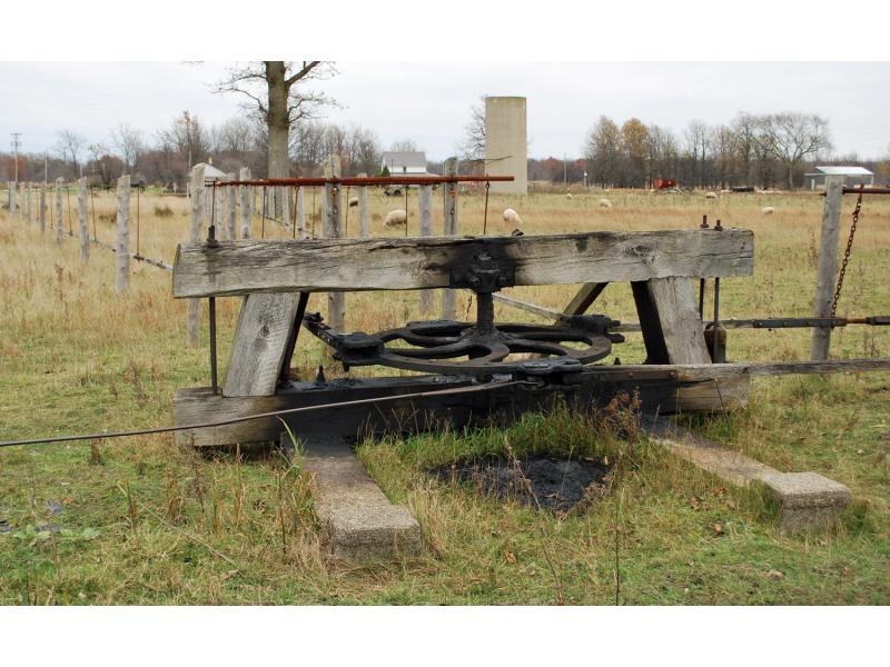 A metal wheel laying vertical to the ground held up by wooden supports. It is connected to jerker lines that are leading off in different directions across a field.