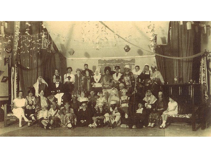 A group of people inside a room with curtains along the walls. They are dressed up in costumes and there are decorations hanging from the ceiling.