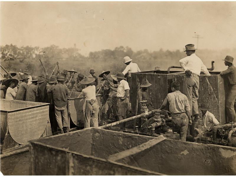Bloss Sutherland and George York look on as a group of native labourers mix cement in a large container.