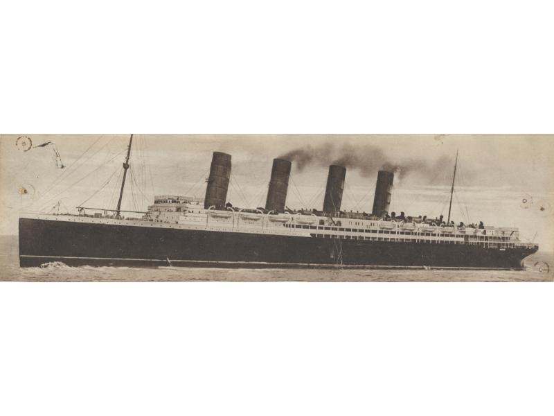A long ship with two masts and four smoke stacks, moving through the water. The body is black and the upper decks are white with life boats hanging from them.