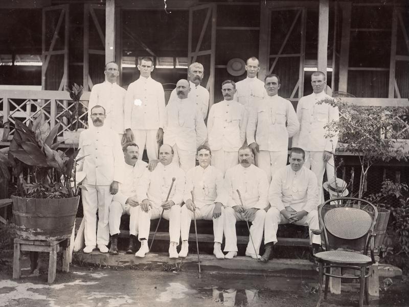 Group photograph of foreign drillers in Borneo all wearing white suits. They are posed in front of a building on a set of steps.