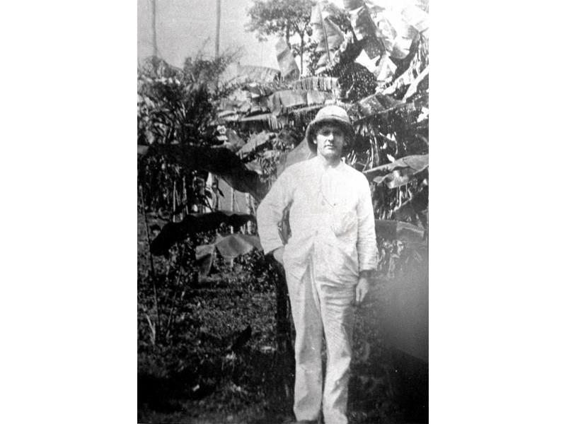Henry Gregory standing in front of a trees. He is wearing a white suit and pith helmet.