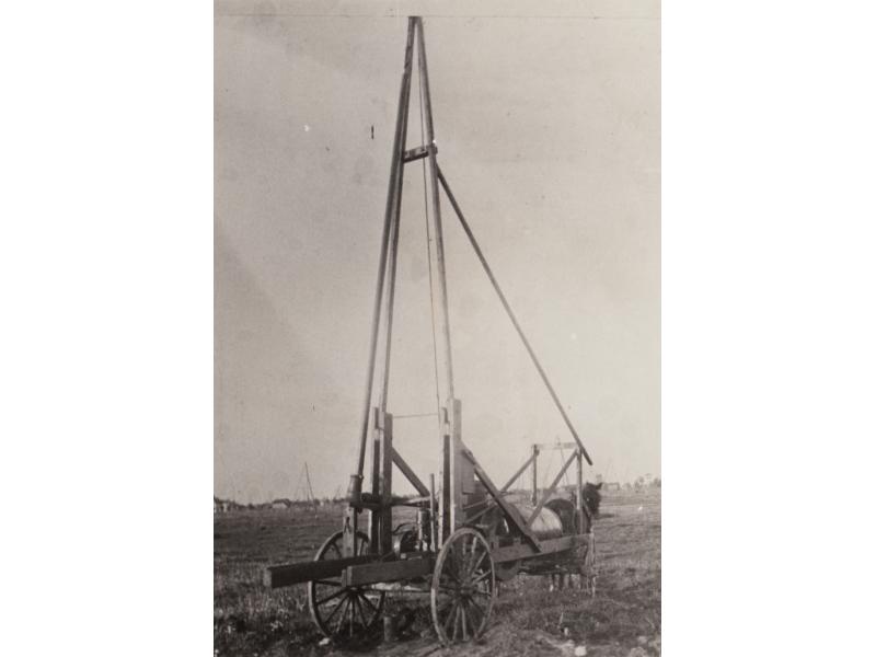 Une machine de trempage de pétrole brut sur une charrette à quatre roues tirée par un cheval. Il y a trois poteaux principaux et un poteau de soutien qui descend vers le cheval.