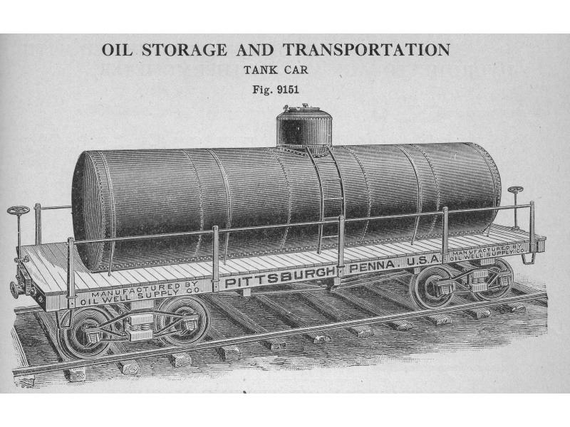 A cylindrical storage tank with a cap on top and ladder leading up to it. It is resting on a railway car with wheels. The car says: "Manufactured by Oil Well Supply Co. Pittsburgh Penna. U.S.A. Manufactured by Oil Well Supply Co."