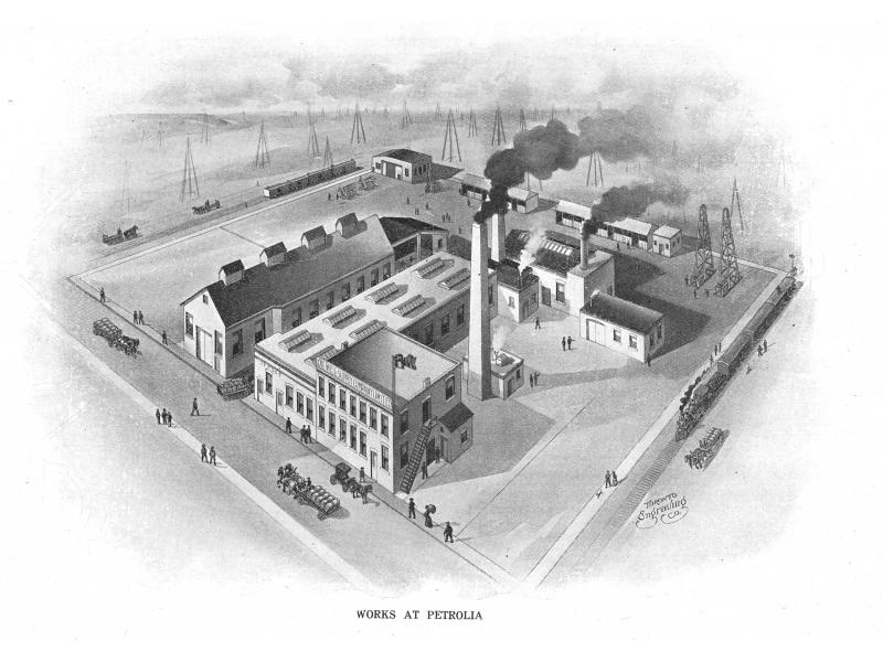 A set of buildings within a square. There is a smokestack in the middle. There are oil derricks in the background.