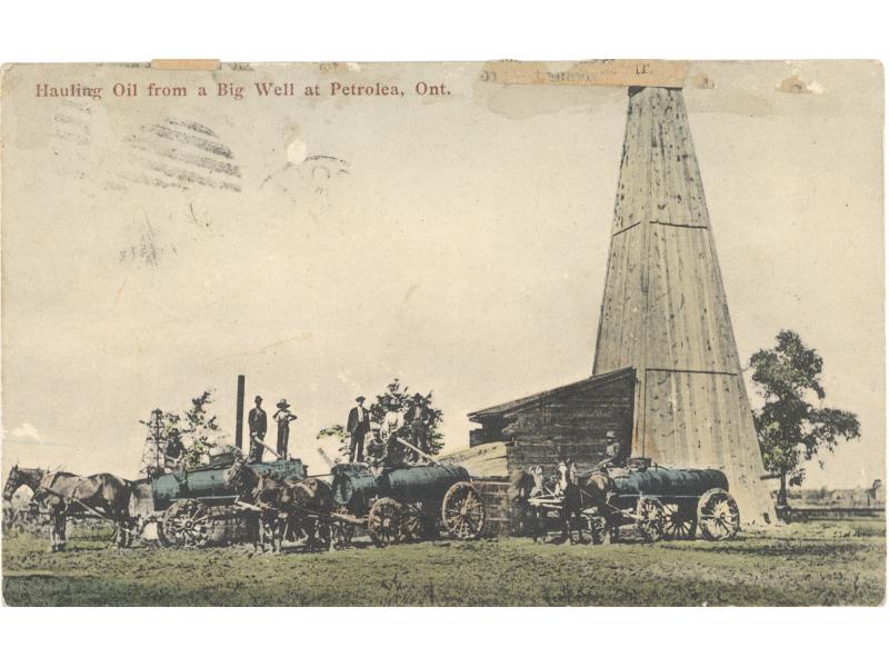 A group of men stand on storage tanks behind three teams of horses pulling tank wagons. There is an oil rig covered in wood planks behind them.