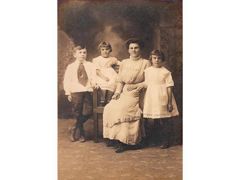 Mme Humphrey Tracy avec ses trois enfants. Elle est assise sur une chaise large avec son plus jeune et les deux autres enfants sont debout. Ils sont tous vêtus de blanc.