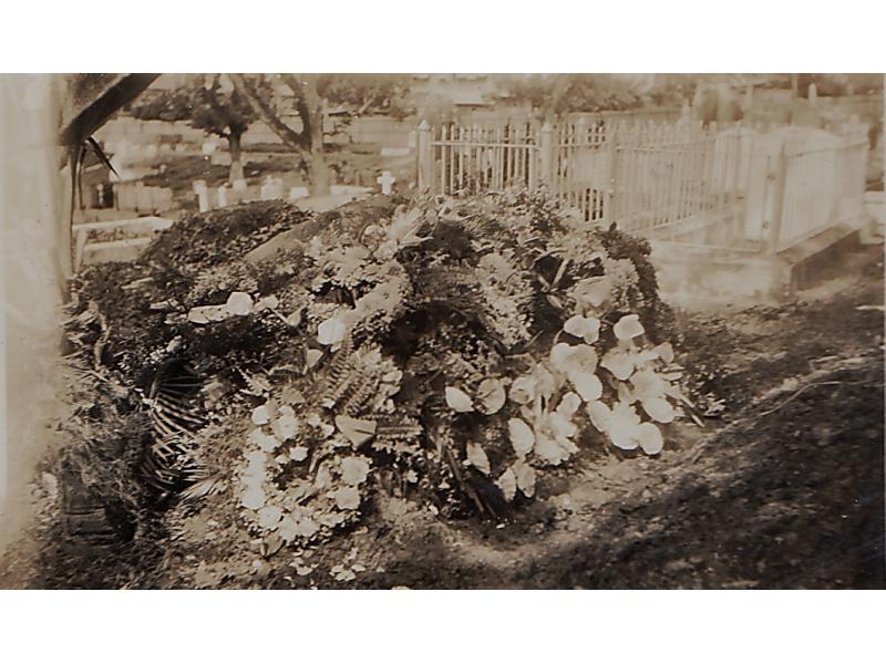 A photo of a mound of earth covered in flowers in a cemetery. There are tombstones in the background.