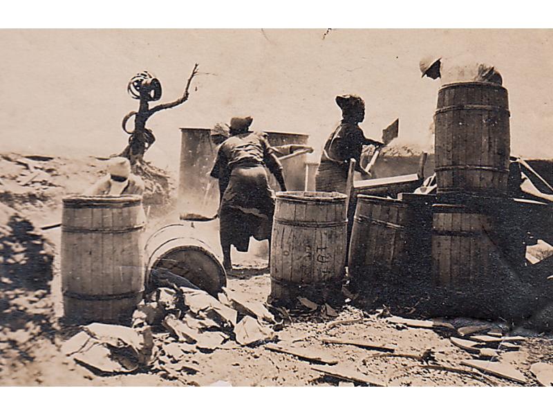 Five people surrounded by barrels and shoveling cement to build up a well.