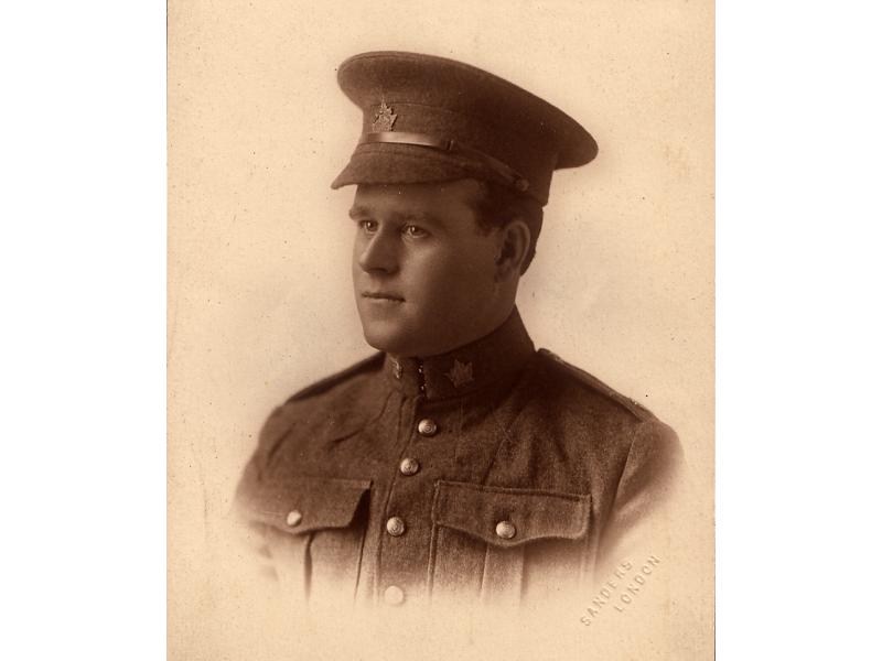 Harry Brown porte un uniforme militaire avec un insigne de feuille d'érable sur le col de sa veste et sur son chapeau. Il est rasé de près et a un visage rond.