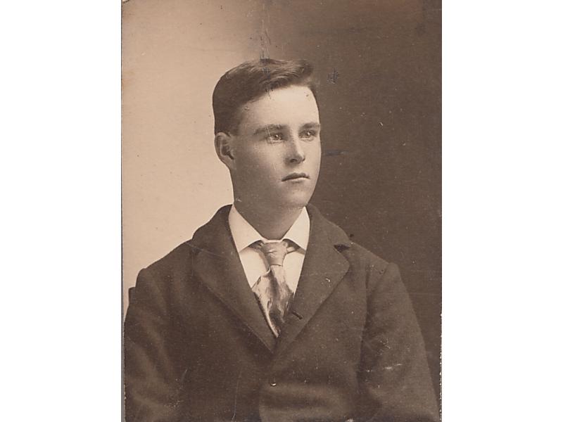 A photo of Harry Brown in his youth. He is wearing a tie and a dark jacket. His hair is combed to one side.