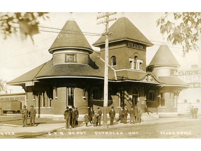 A group of people standing outside a building with two corner turrets and a tower in the centre. There is a hydro pole in front of the middle tower.