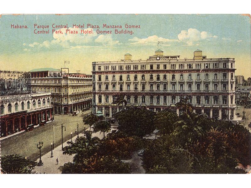 Une carte postale montrant trois grands bâtiments avec de nombreuses fenêtres. Ils sont autour d'une place avec des arbres sur celle-ci. Le ciel est bleu avec des nuages. La carte indique : « Habana. Parque Central, Hotel Plaza, Manzana Gomez. Parc central, Hôtel Plaza, Édifice Gomez. »