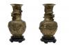 A pair of brass urns sitting on wooden bases. Each vase has a design of two dragons or serpents that is raised off of the urns. There is a serpent wrapped around the neck of both.