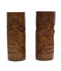 Two carved brown wooden vases. There are images carved into the vases of three bearded men standing near a roofed structure with a tree in the background. The relief images on the vases are mirror images of each other.