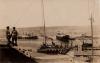 Photo de deux hommes en uniforme debout sur une colline qui mène à un port où sont amarrés trois gros bateaux. Il y a des collines en arrière-plan. 