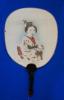 A white fan with a black handle spread open on a blue background. There is an image of a Japanese woman in traditional clothing, from the waist up, printed on the fan. 