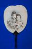 A white fan with a black handle on a blue background. The image of two Japanese women in traditional clothing, from the waist up, is printed on the fan.  