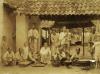 A group of people under an open structure with a tiled roof. There are boards and bowls in front of them and they are preparing food. 