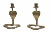 Pair of matching candlesticks in the shape of a cobra snake with its head raised. The candlesticks have been incised with a scale pattern. The candle holder sits on tops of a base coming up from the cobra's head and is decorated with diagonal lines.