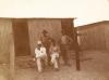 Four men in front of a small building. Campbell and Gillespie are seated, while Gardiner and Kerby are standing. They are wearing an assortment of work clothes.