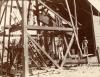 William Gillespie and his workers underneath a wooded rig on Jubal Island. Gillespie is wearing white pants and a pith helmet. 